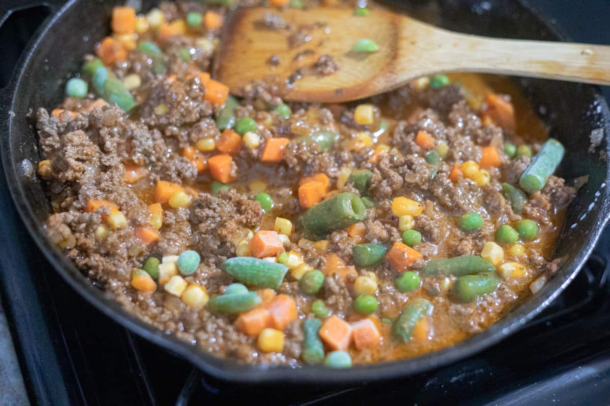 Beef, gravy, and vegetables cooking in a pan.