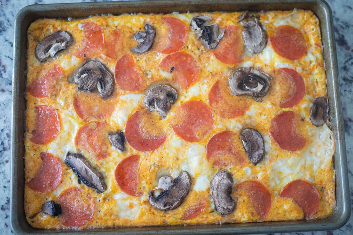 Cooked eggs in a sheet pan topped with mushrooms and pepperoni. 