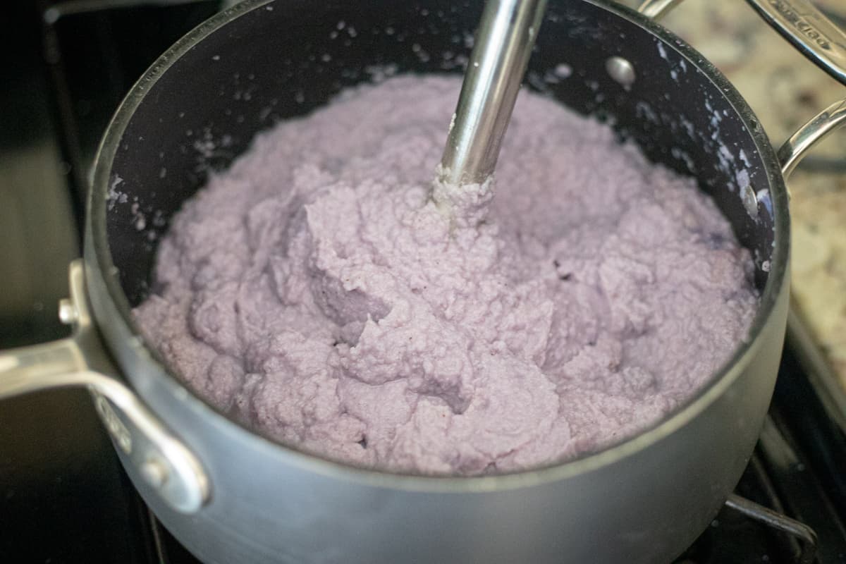 Purple cauliflower being blended with an immersion blender in a saucepan. 