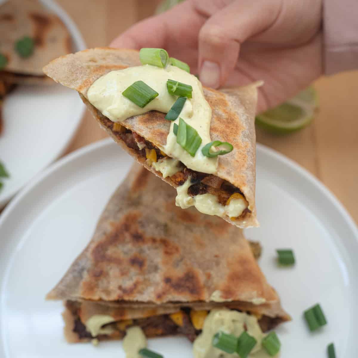 A hand holding a quesadilla that's topped with avocado lime dip. 
