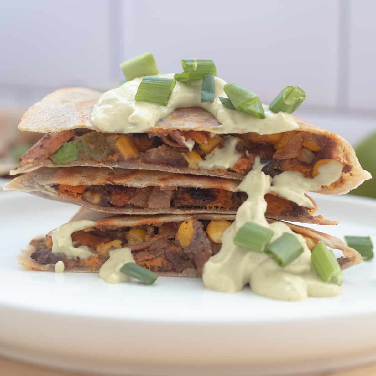 A stack of sweet potato quesadillas topped with green avocado lime dip.