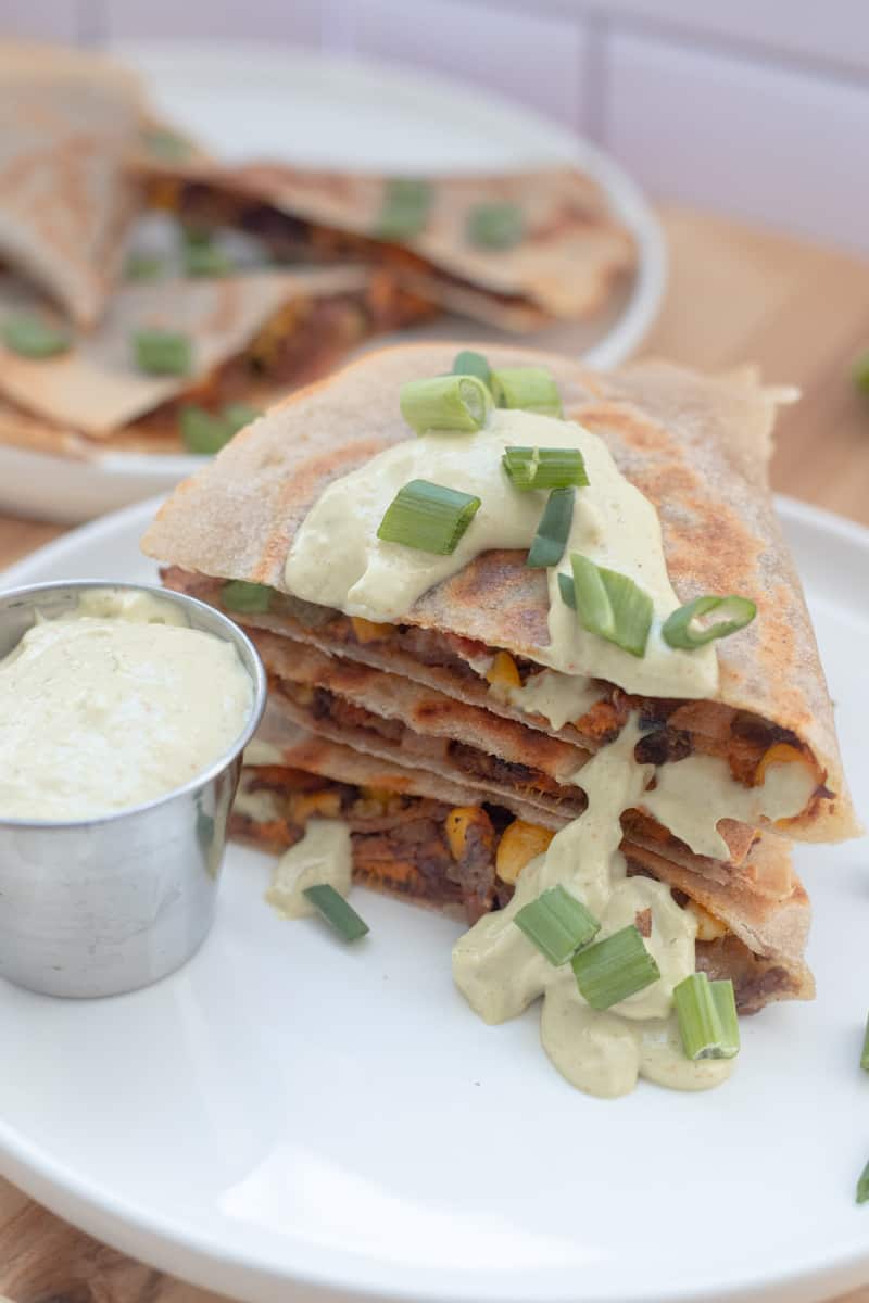 A stack of sweet potato quesadillas topped with green avocado lime dip. 
