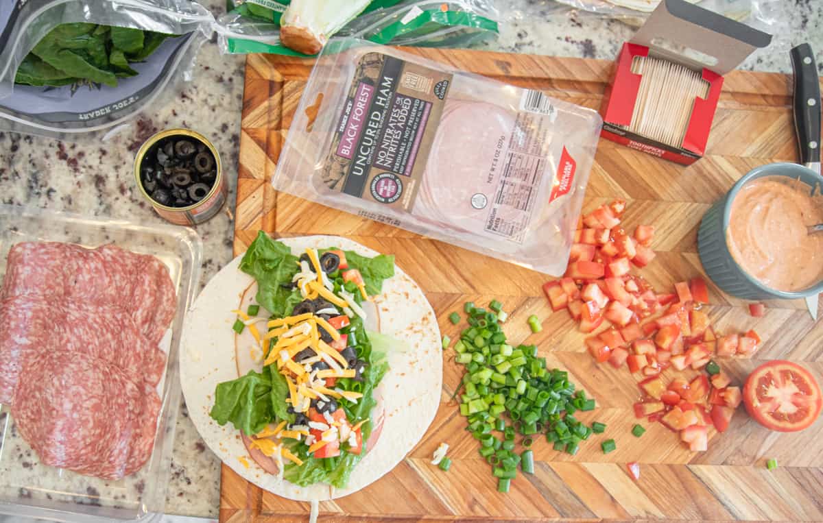 A cutting board filled with roll up ingredients, and a tortilla loaded with toppings down the middle. 