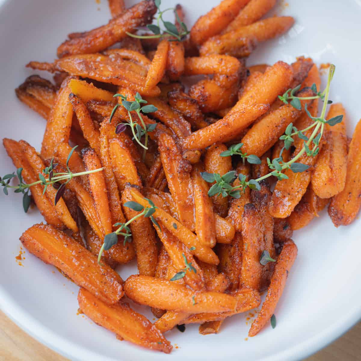 Air fryer baby carrots in a serving bowl topped with green garnish.