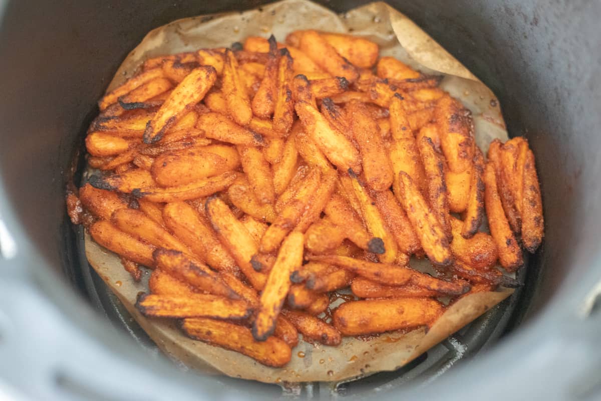 Cooked baby carrots in an air fryer basket. They're slightly browned on the edges. 