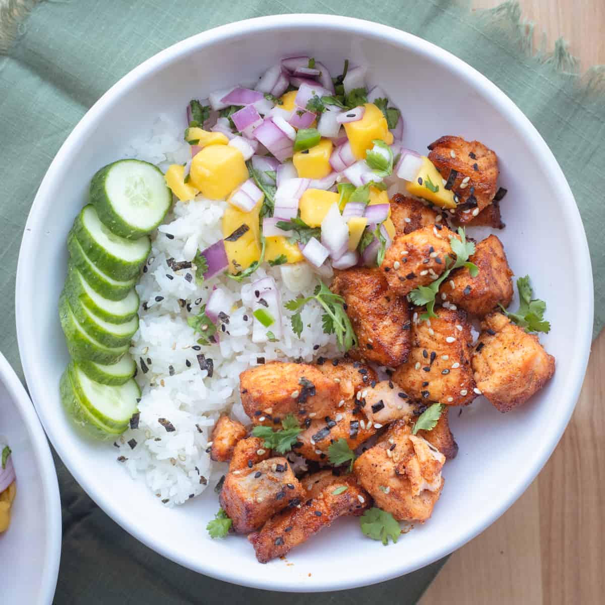 A bowl with salmon bites, rice, mango salsa, and cucumber. 