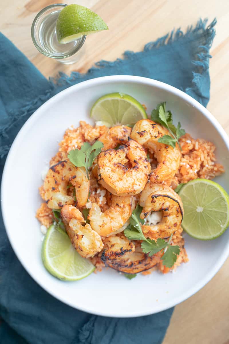 Air fryer tequila lime shrimp over rice with limes on the side.