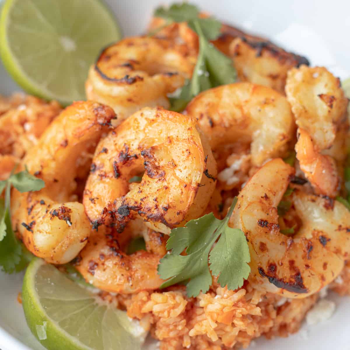 Air fryer tequila lime shrimp over rice with limes on the side.