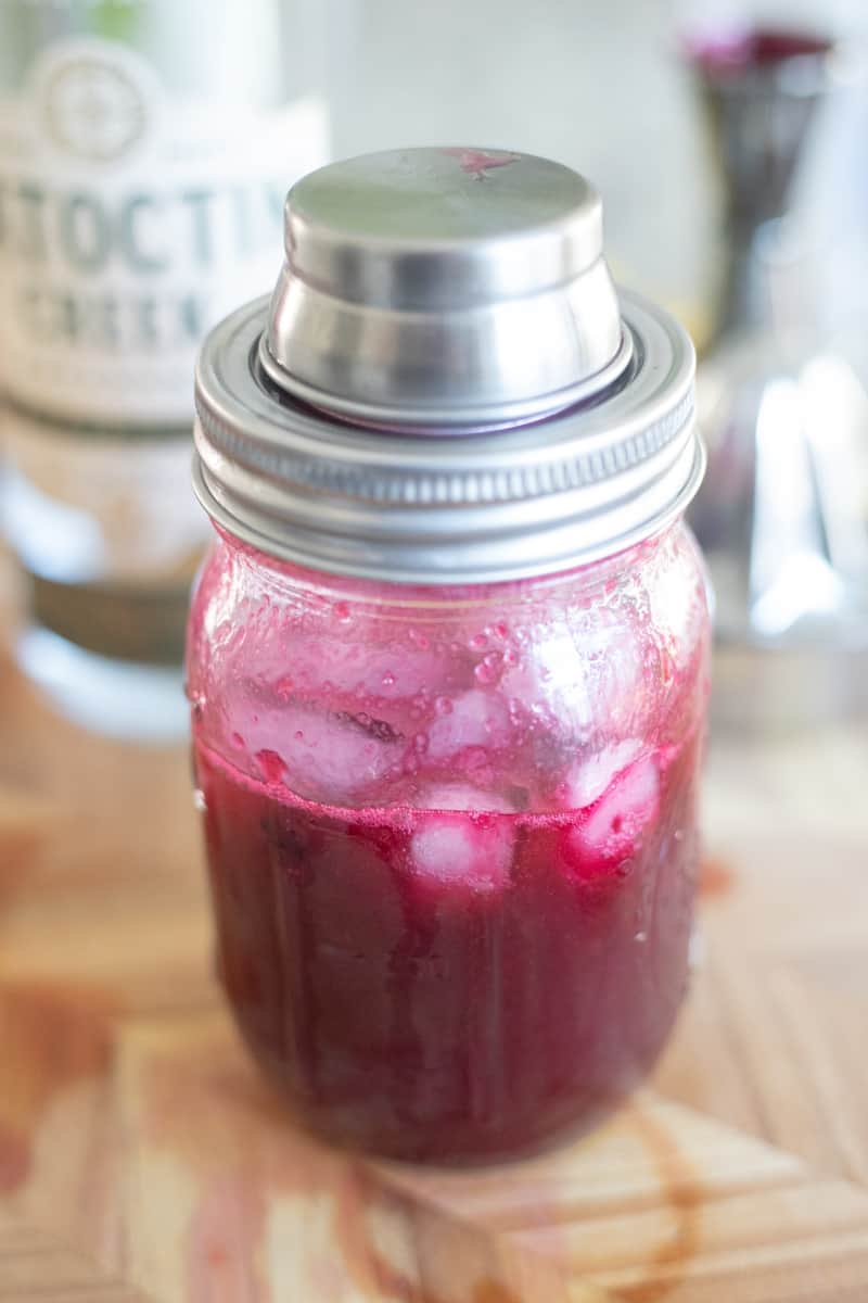 A cocktail shaker filled with ice, blueberry syrup, gin, lemon, and simple syrup. 