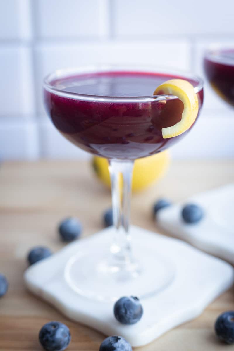 A coupe glass filled with blueberry gin cocktail. 