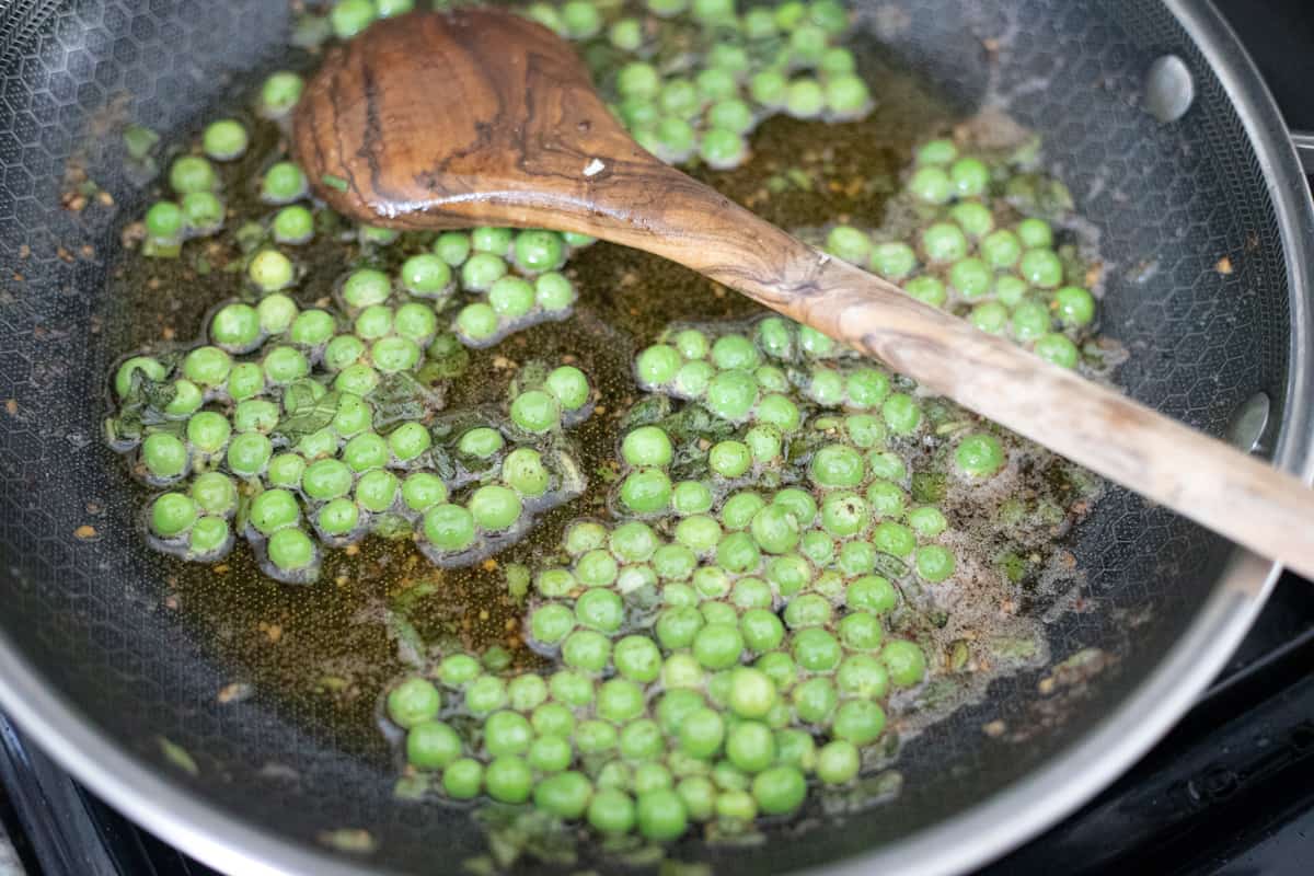 Peas cooking in brown butter in a pan. 