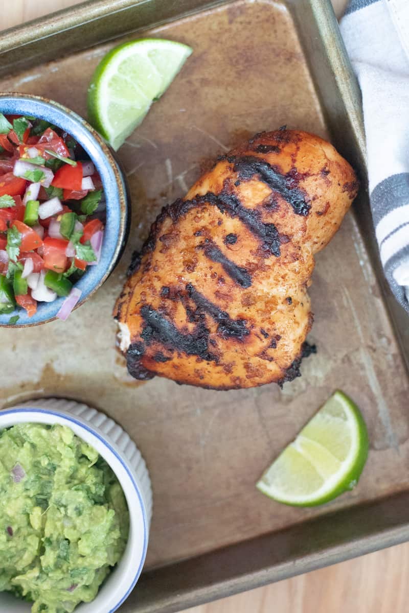 Grilled margarita chicken resting on a sheet pan next to pico de gallo and guacamole. 