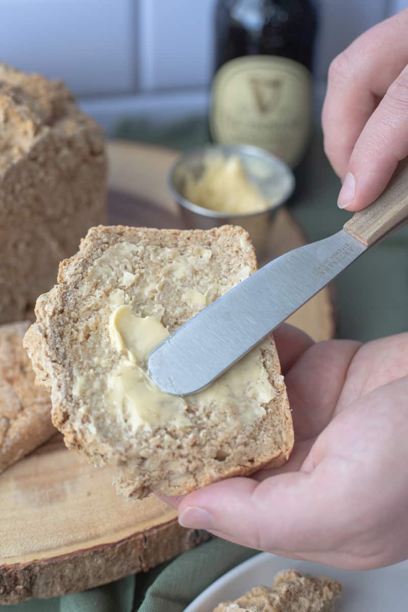 A slice of Guinness beer bread being slathered with butter.