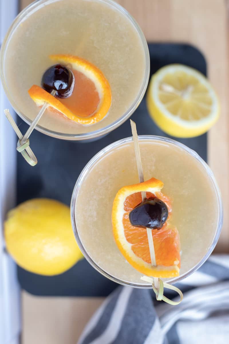 An overhead view of a whiskey sour in a couple glass garnished with an orange peel and a cherry. 