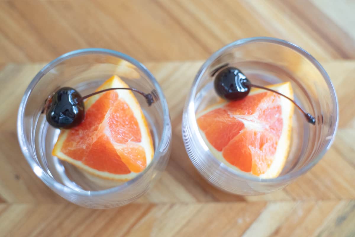 Two lowball glasses with an orange slice and a cherry. 