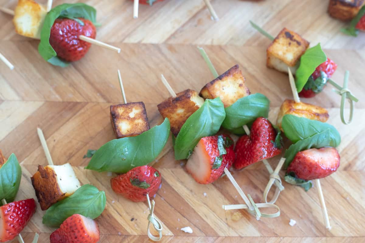 Skewers with strawberry, basil, and halloumi cheese on a cutting board. 
