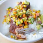 Air fryer blackened salmon on top of a bowl of rice. It is topped with a corn and mango salsa.