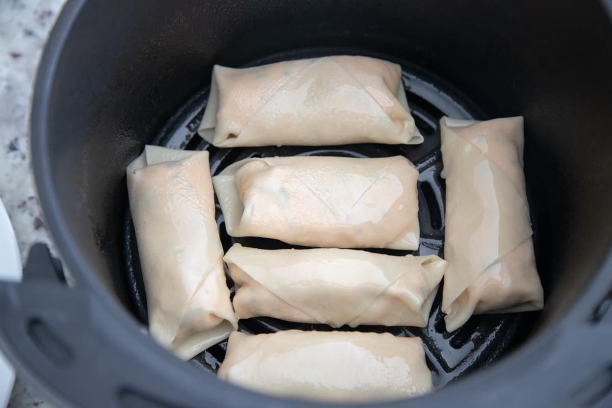 Uncooked buffalo chicken egg rolls in an air fryer. There are six in the fryer, and they're not touching. 