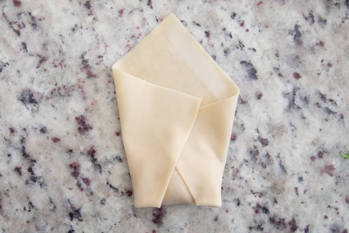 An egg roll wrapper filled with filling. The bottom corner and two side corners are folded toward the middle. 