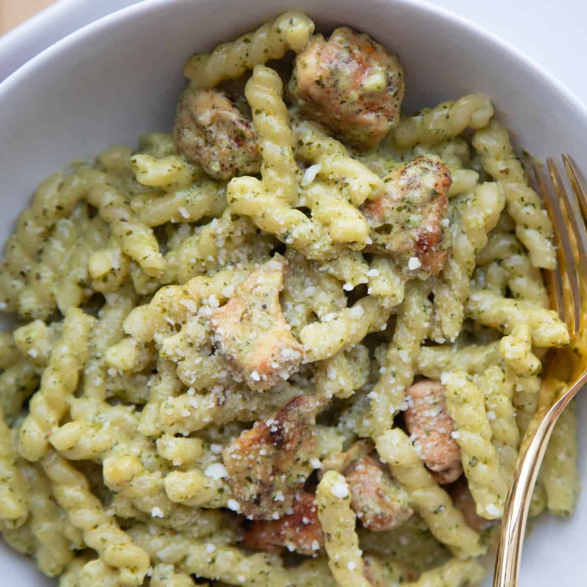 Creamy pesto pasta with chicken in a bowl with a fork on the side. The pasta is light green in color and topped with parmesan cheese.