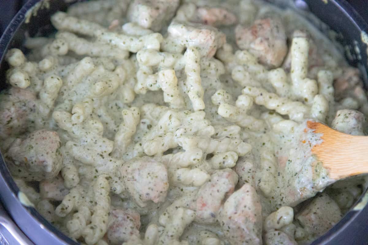 Pasta, creamy pesto sauce, and cooked chicken mixed together in a pan. 