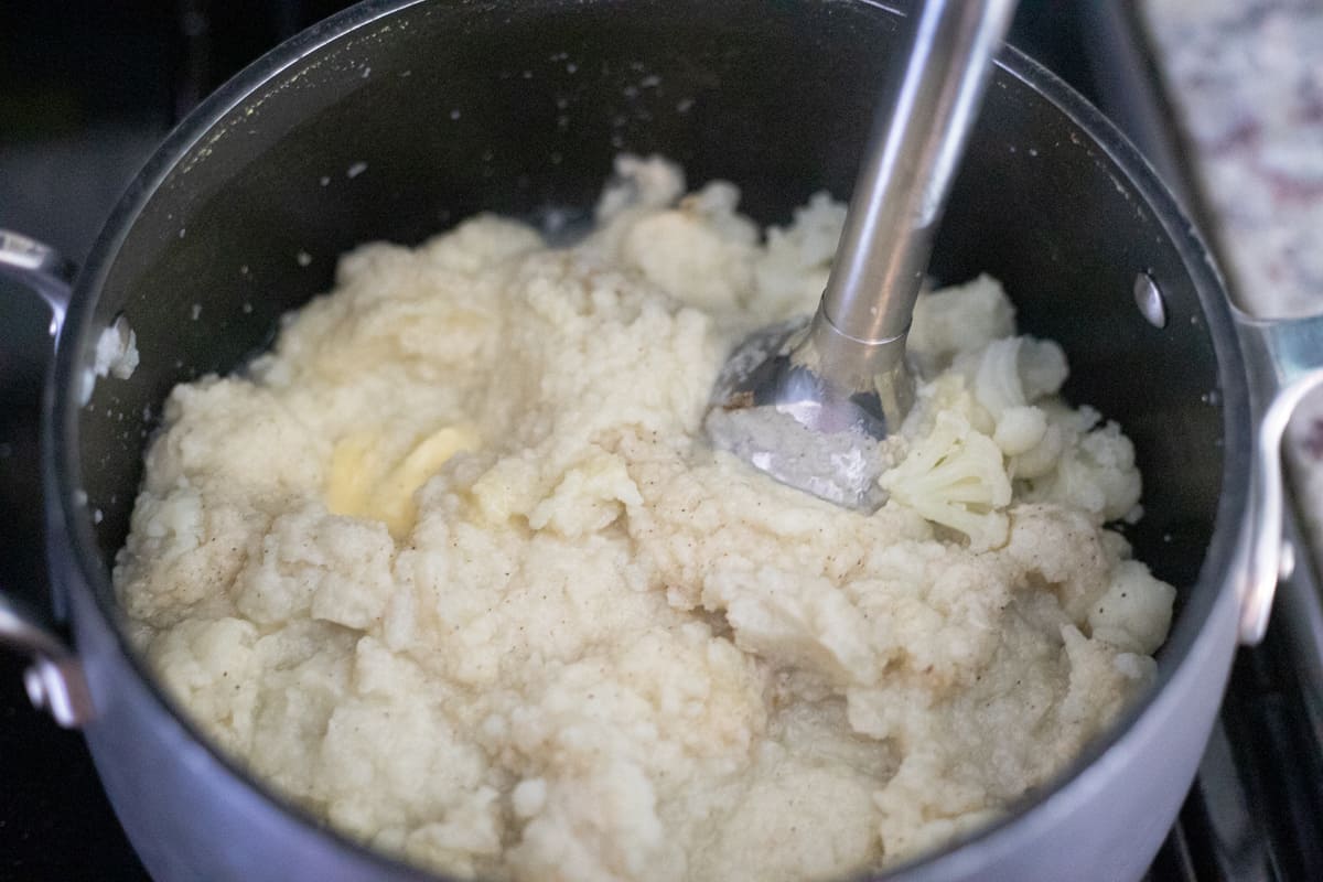 An immersion blender blending cauliflower in a pot. 