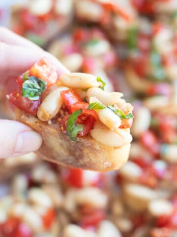 A hand holding a piece of french bread topped with white bean bruschetta.