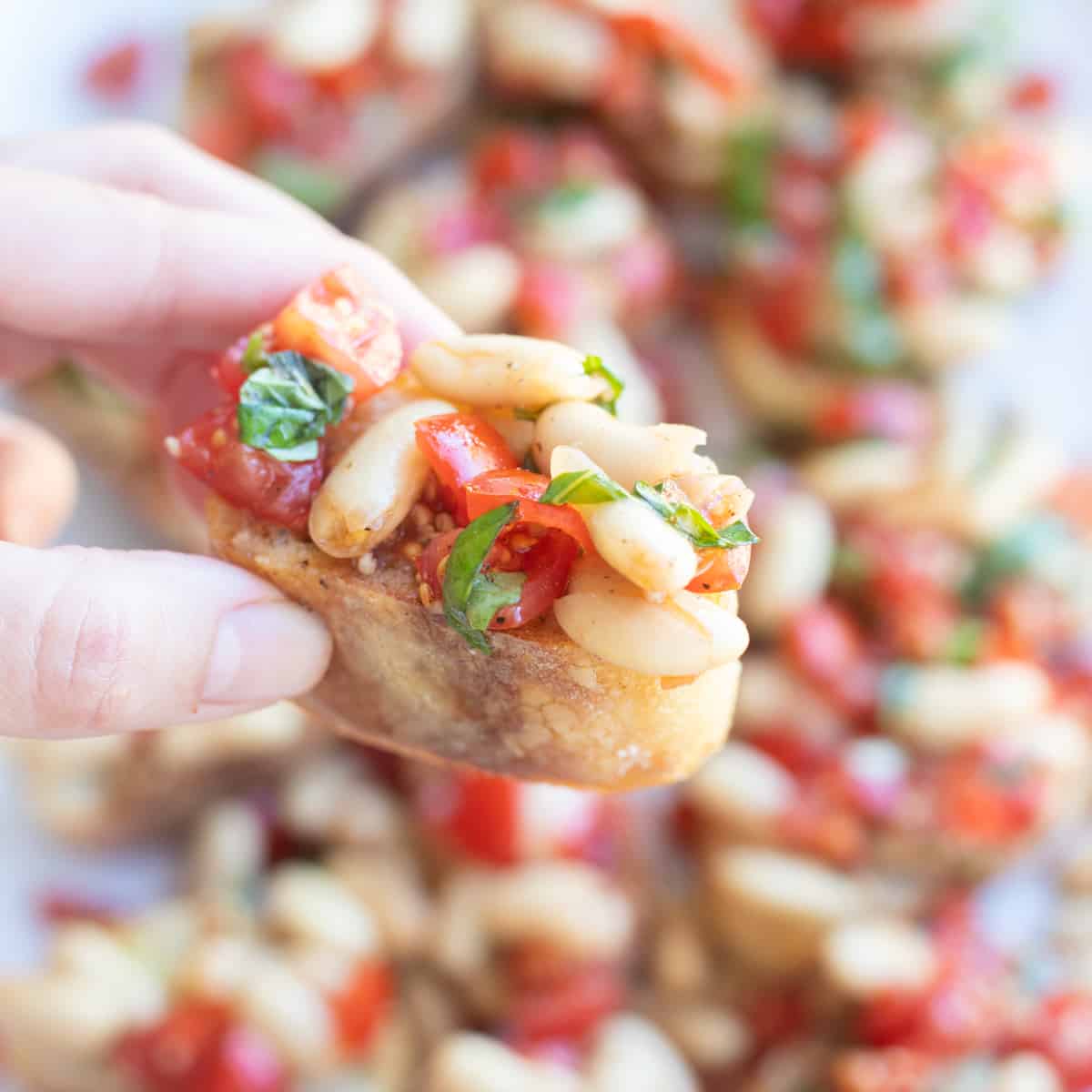 A hand holding a piece of french bread topped with white bean bruschetta. 