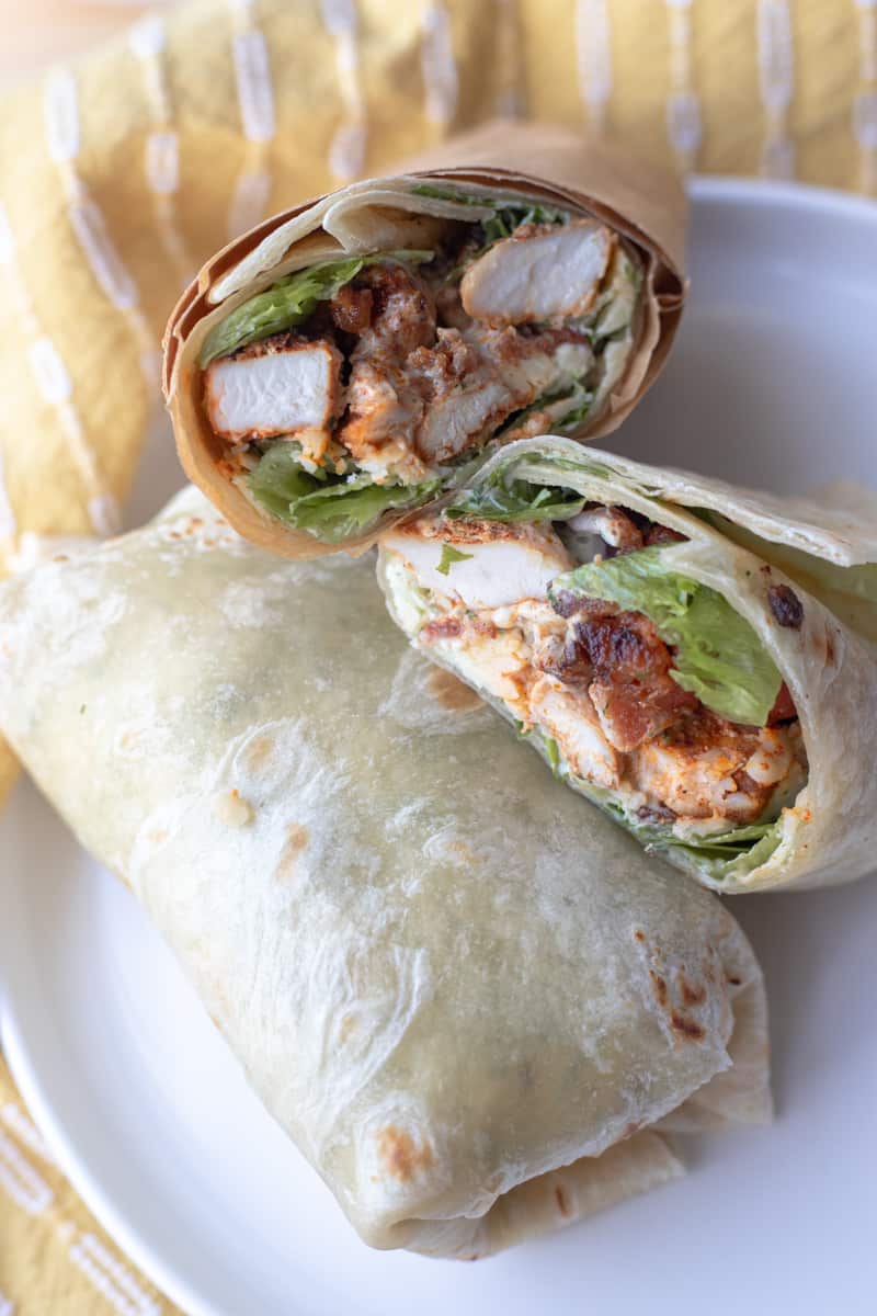 An air fryer chicken wrap on a plate with a cut open air fryer chicken wrap propped on top of it. It's dipped in cilantro lime ranch.