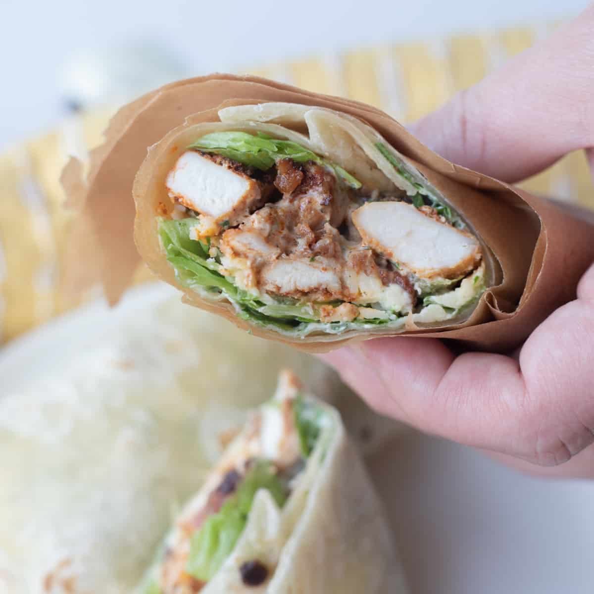A hand holding an air fryer chicken wrap. It's wrapped in parchment paper.