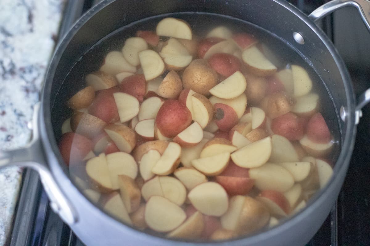 Quartered baby potatoes cooking in a saucepan with water. 