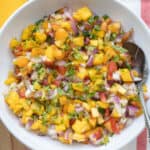 Mango peach salsa with tomatoes in a serving bowl with a spoon.