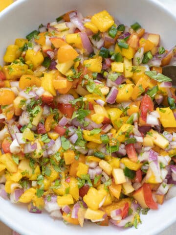 Mango peach salsa with tomatoes in a serving bowl with a spoon.