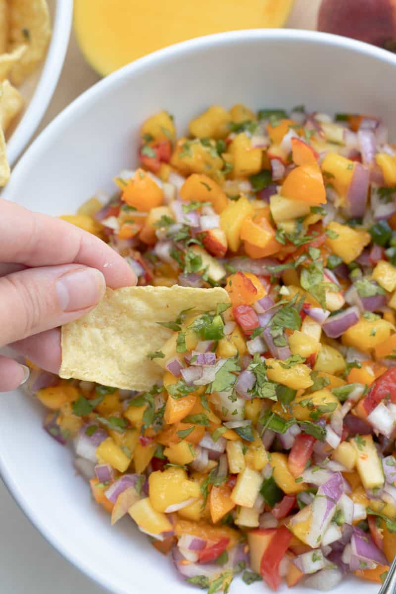 Mango peach salsa in a mixing bowl with a tortilla chip being dipped in.