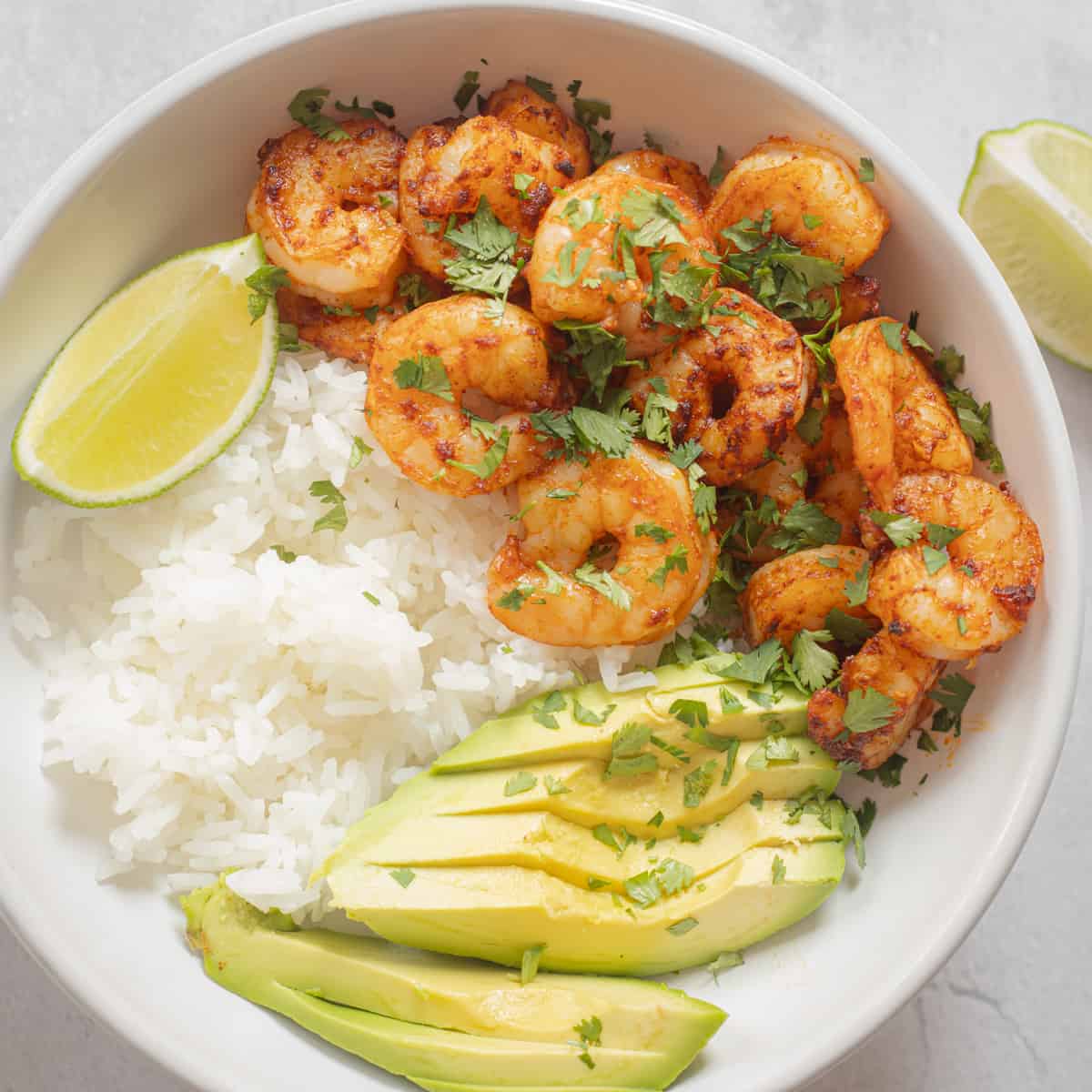 Cooked frozen shrimp in a serving bowl with rice, cilantro, avocado, and lime. 