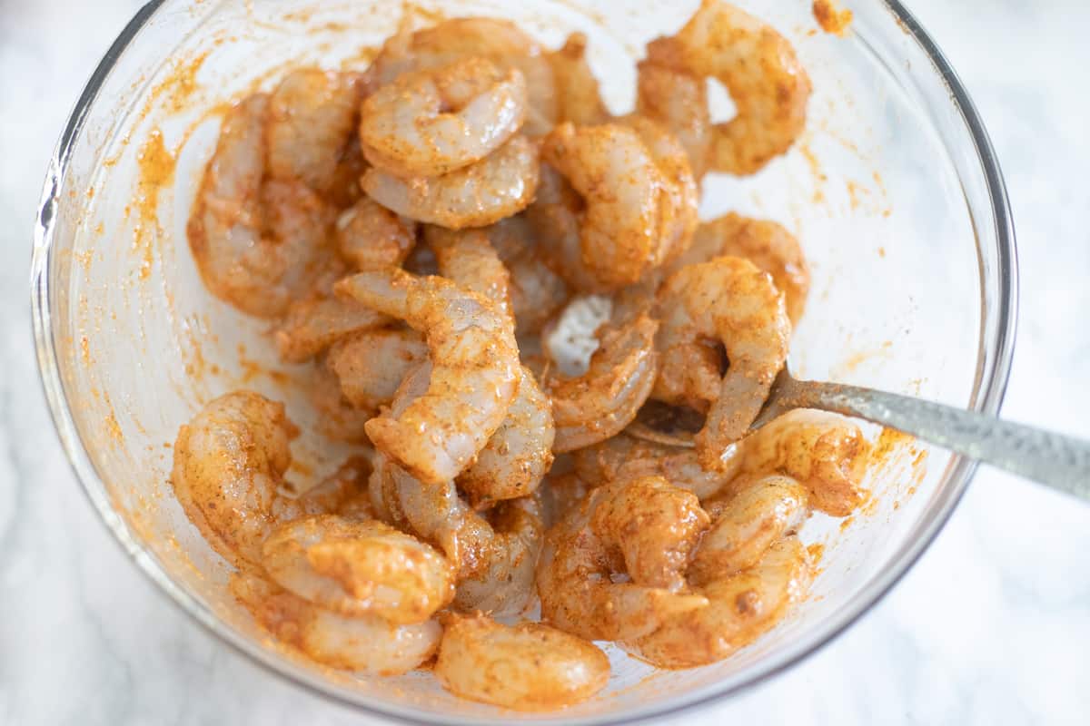 Shrimp coated with taco seasoning in a mixing bowl. 