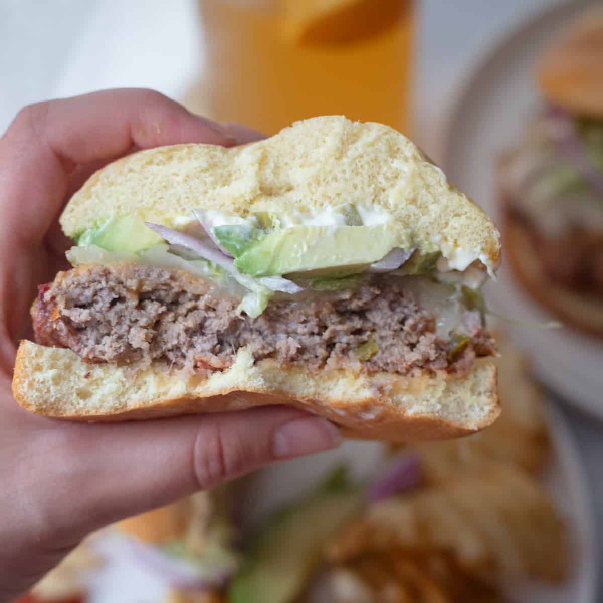 A hand holding a jalapeno cheddar burger that has been cut in half. 