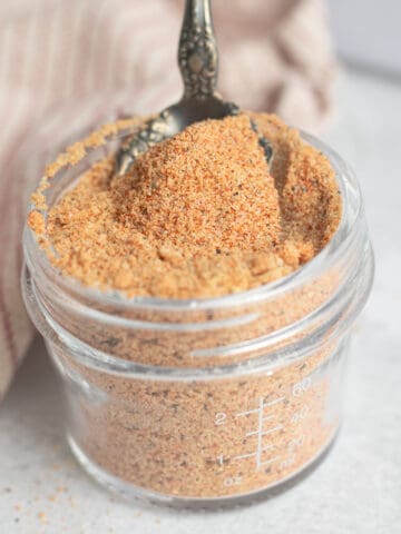 A jar of Kansas City-style BBQ dry rub. A spoon is resting on the top.
