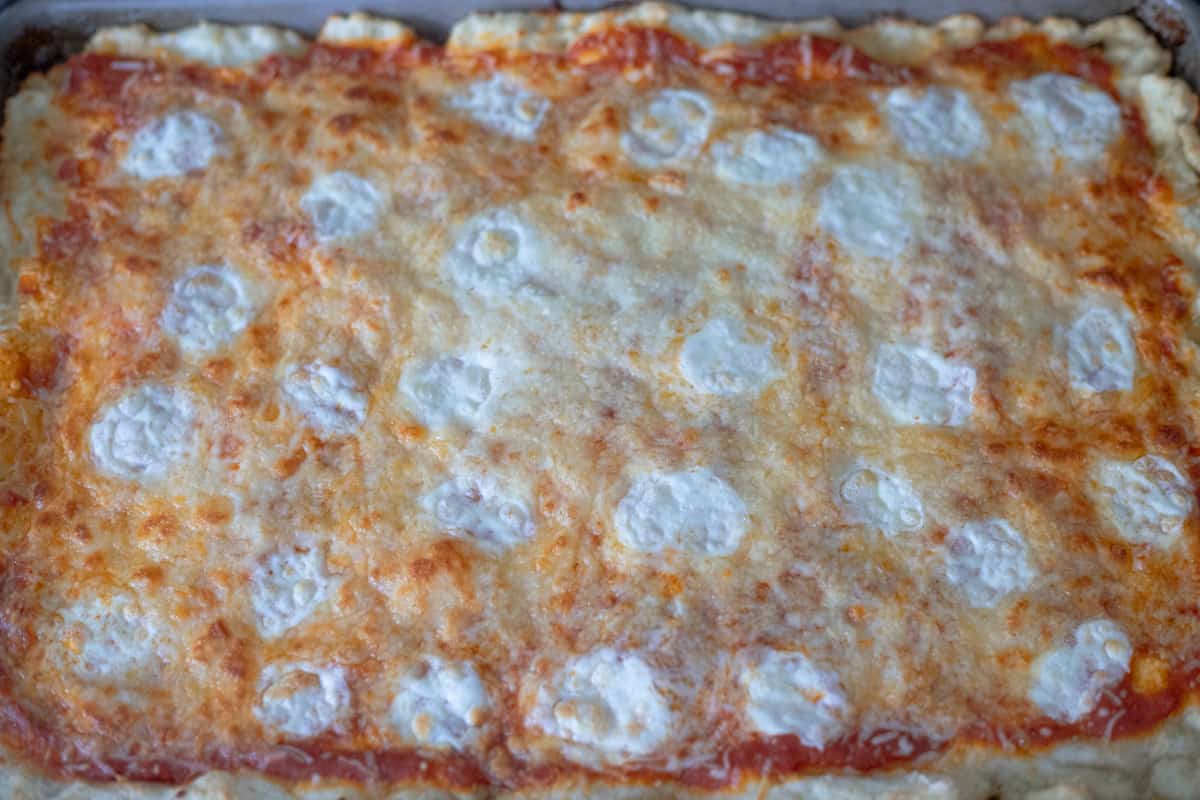 A baked, uncooked pizza in a sheet pan. 