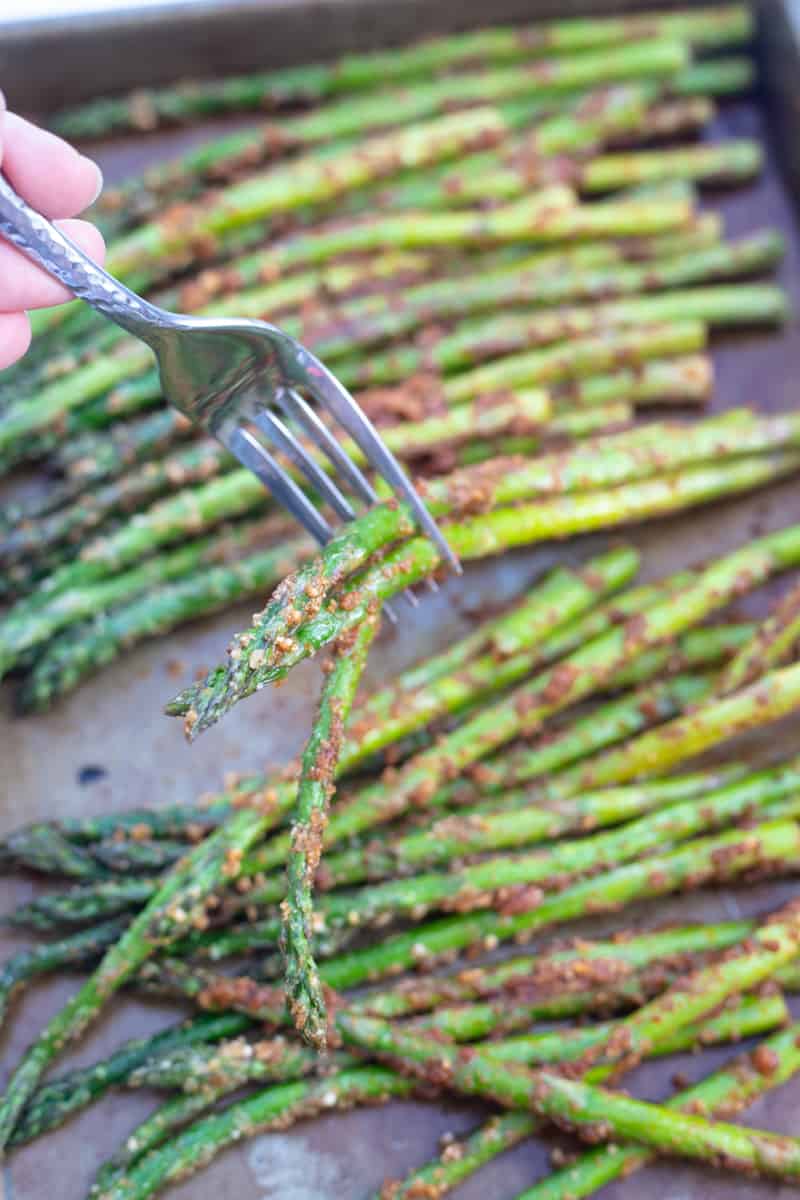 A fork digging into a couple of asparagus spears. 