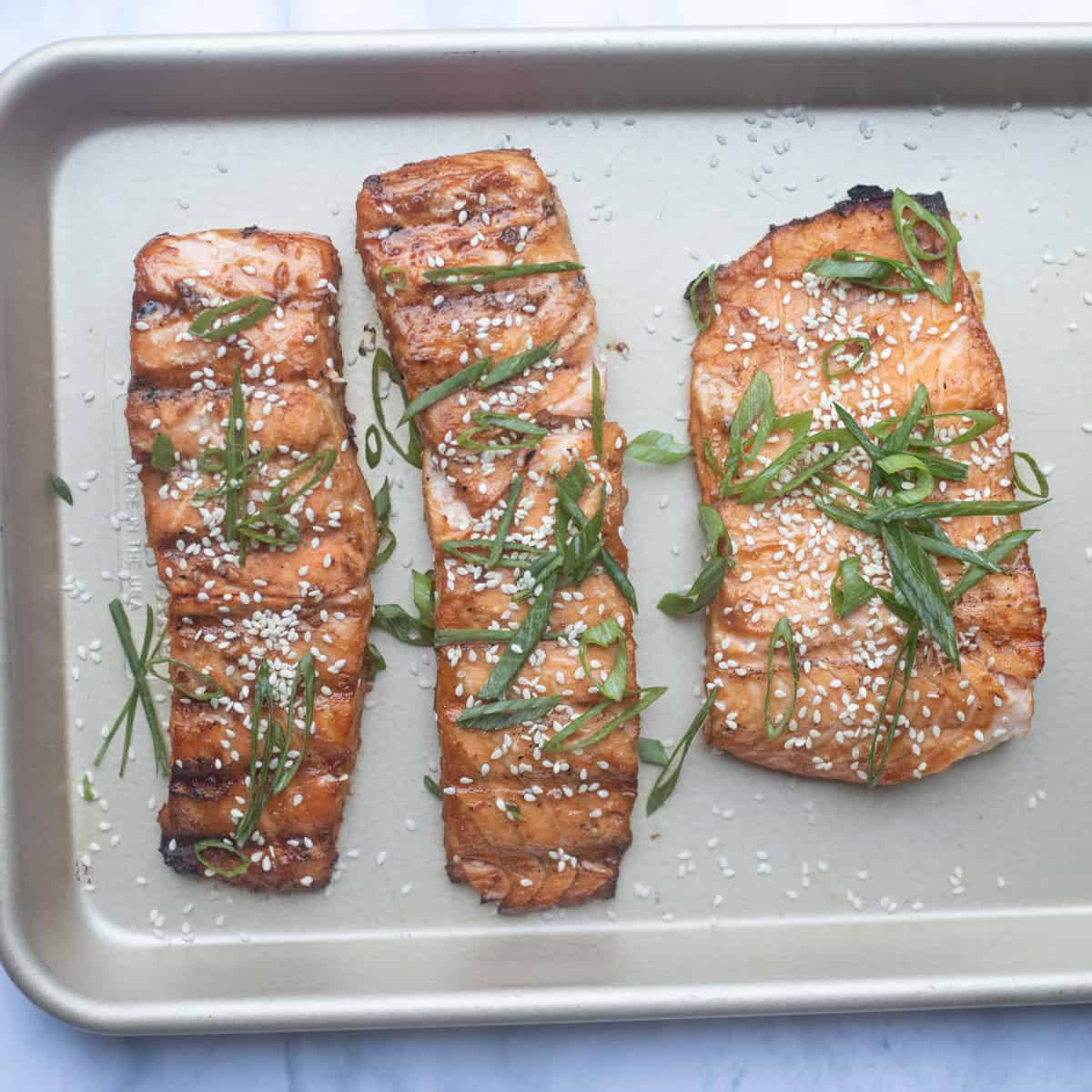 Cooked miso salmon resting on a baking sheet. It is garnished with green onions and sesame seeds. 