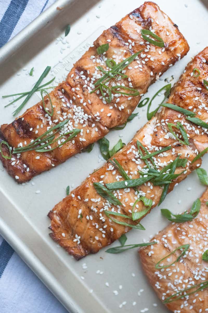 Grilled miso salmon fillets on a baking sheet. They are garnished with green onions and sesame seeds.