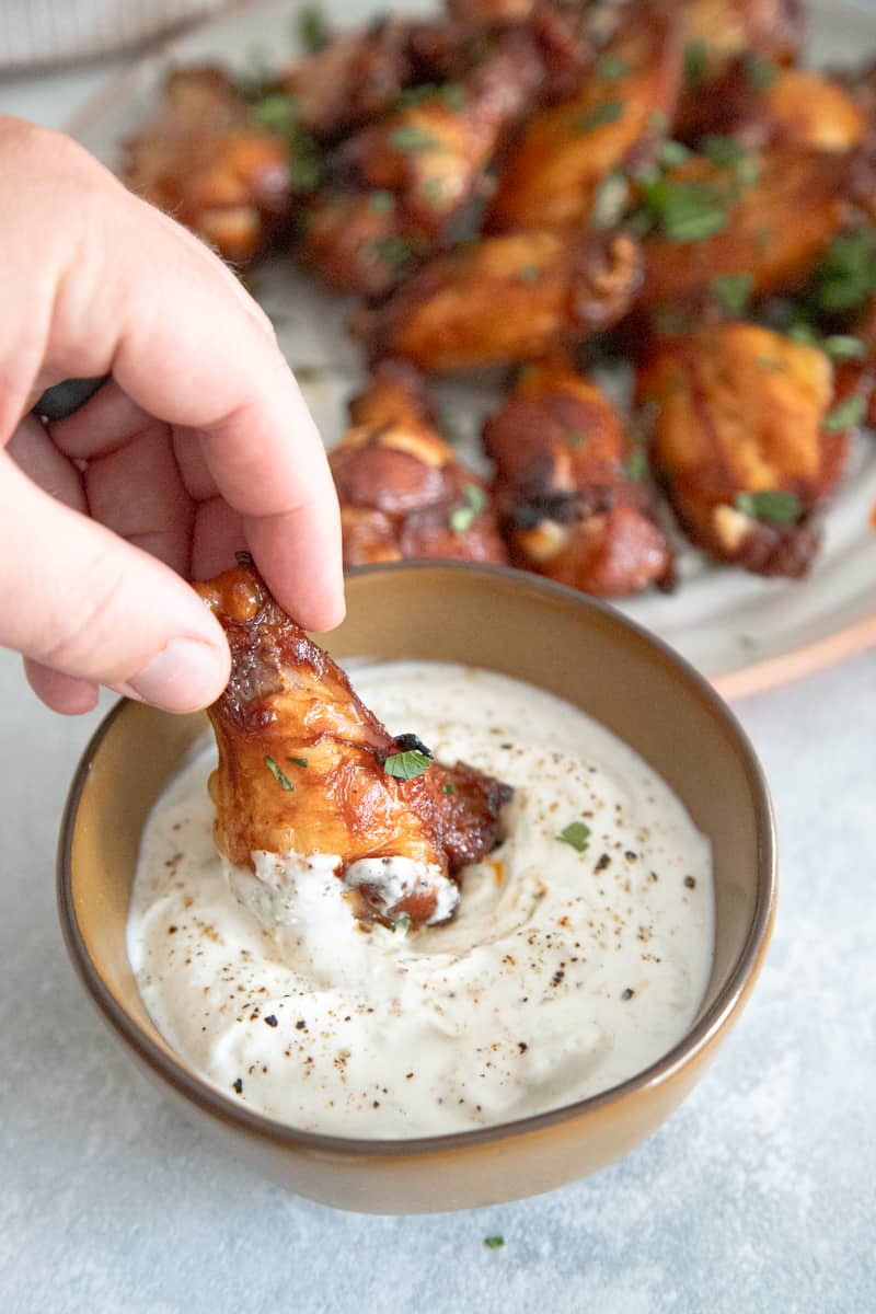 An orange-colored chicken wing being dipped into a bowl of ranch dressing. 