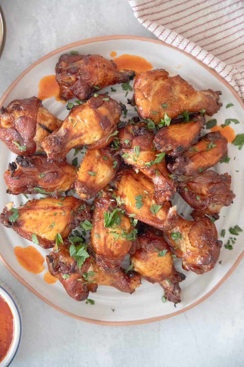 Chicken wings on a plate. They're covered in an orange hot sauce and topped with green garnish. 