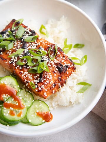 Miso salmon in a serving bowl on top of rice. It's garnished with green onions and sesame seeds.