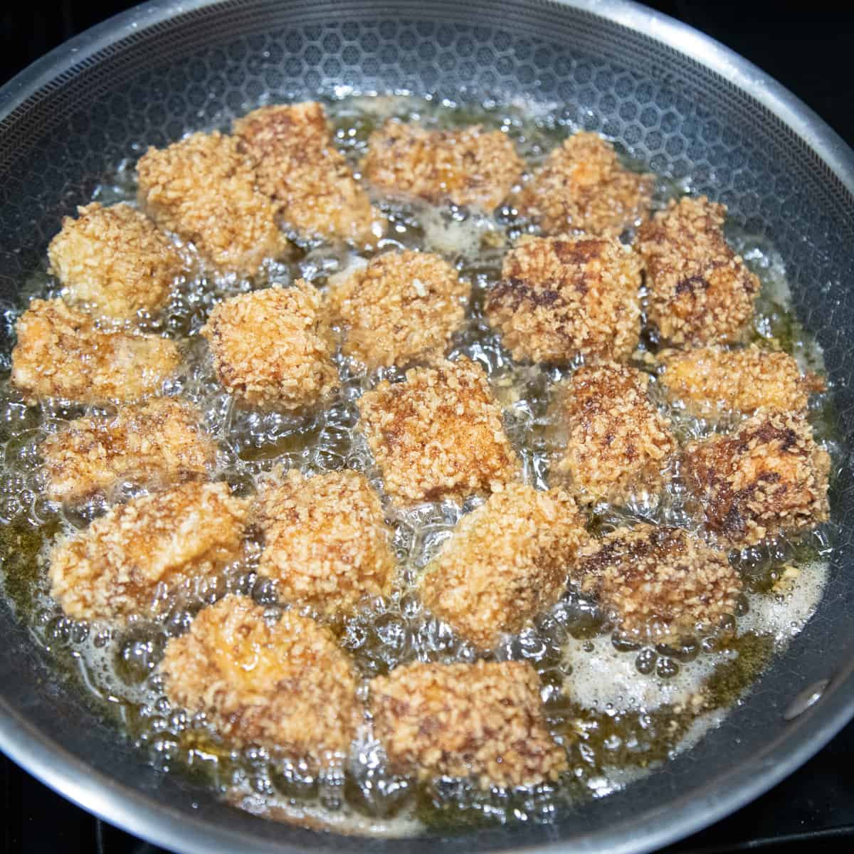 Breaded salmon frying in a pan. It is cooked on one side and golden-brown in color. 