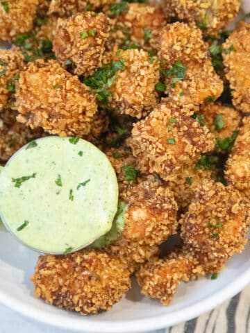 A bowl of salmon nuggets. They're golden brown and served next to a bowl of basil dipping sauce.
