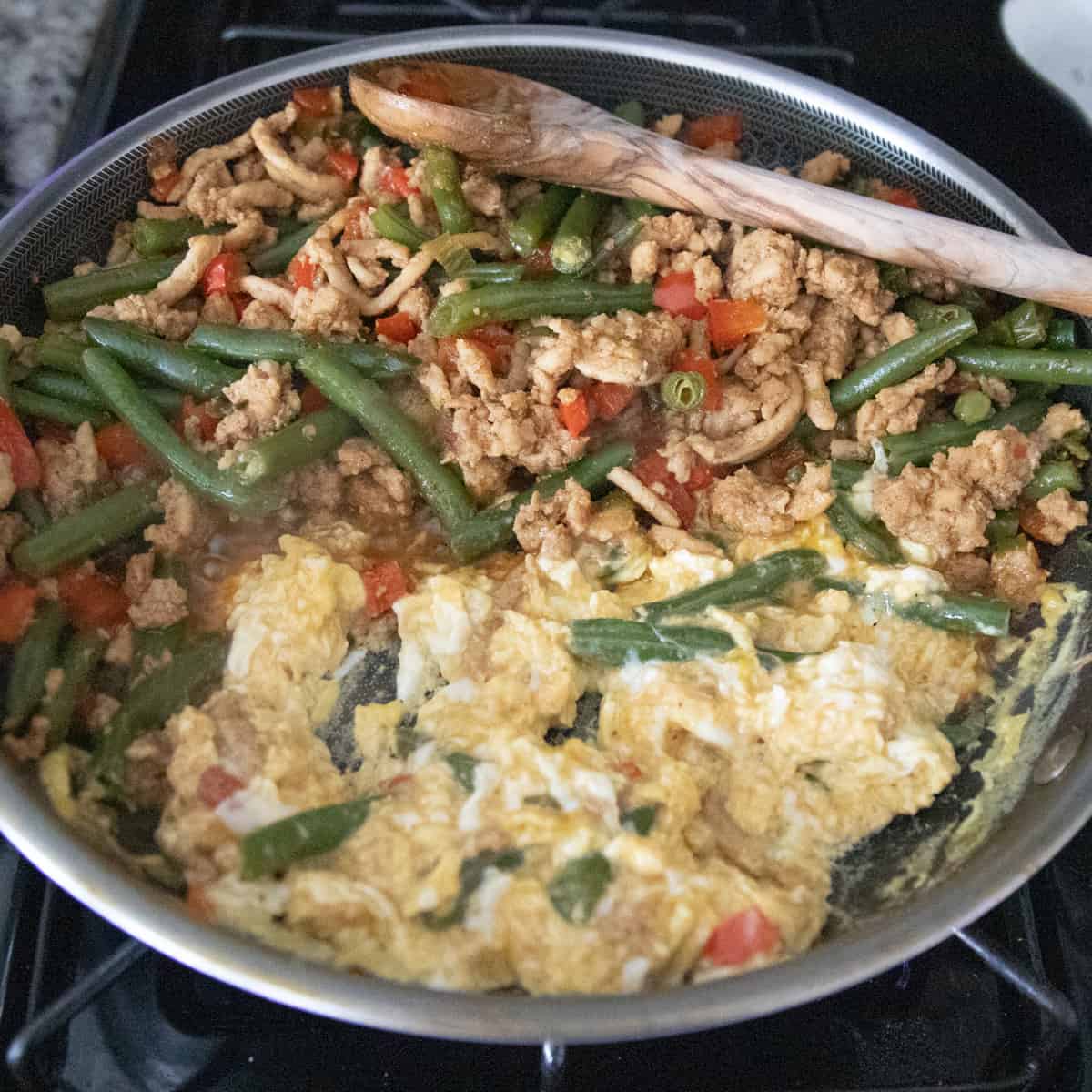 Ground chicken and vegetables on one side of a pan and scrambled eggs on the other side. 