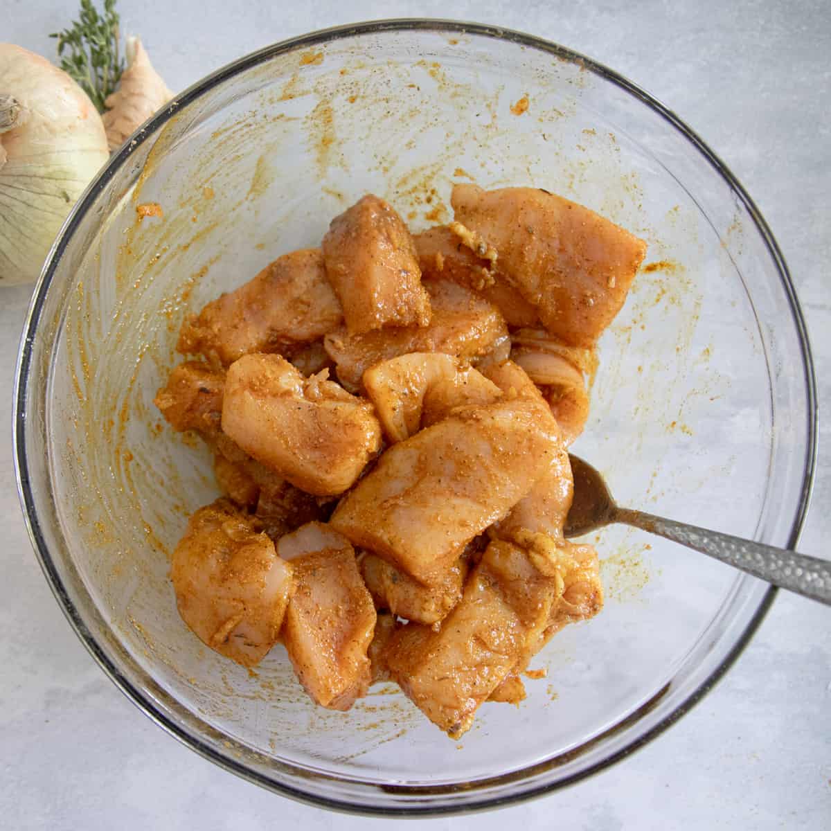 Chunks of chicken in a mixing bowl with seasonings. 