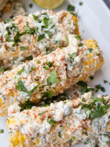 A plate of Mexican street corn topped with cilantro and garnished with lime slices on the side.